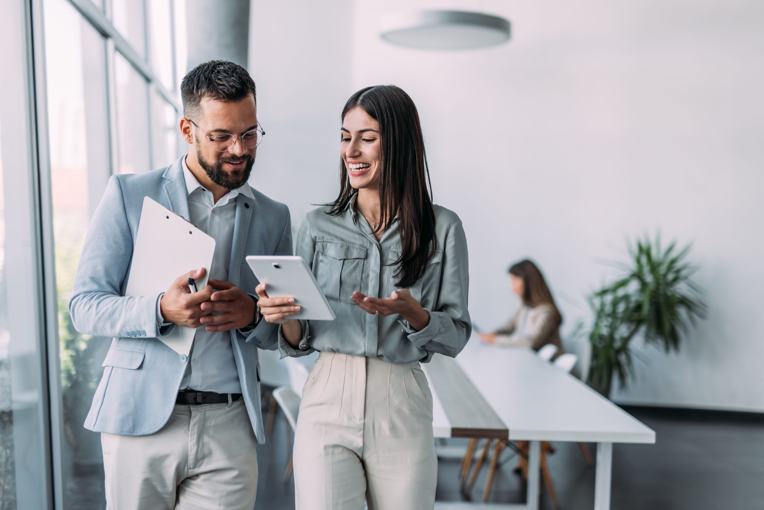 Shot of a two confident business persons talking in the work place. Two colleagues using a digital tablet while walking in a modern office. Businessman and businesswoman in meeting discussing business strategy. Business coworkers working together in the offic